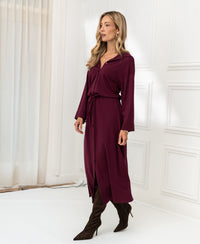Woman wearing a Bordeaux button-front dress stands in a white room with sheer curtains.
