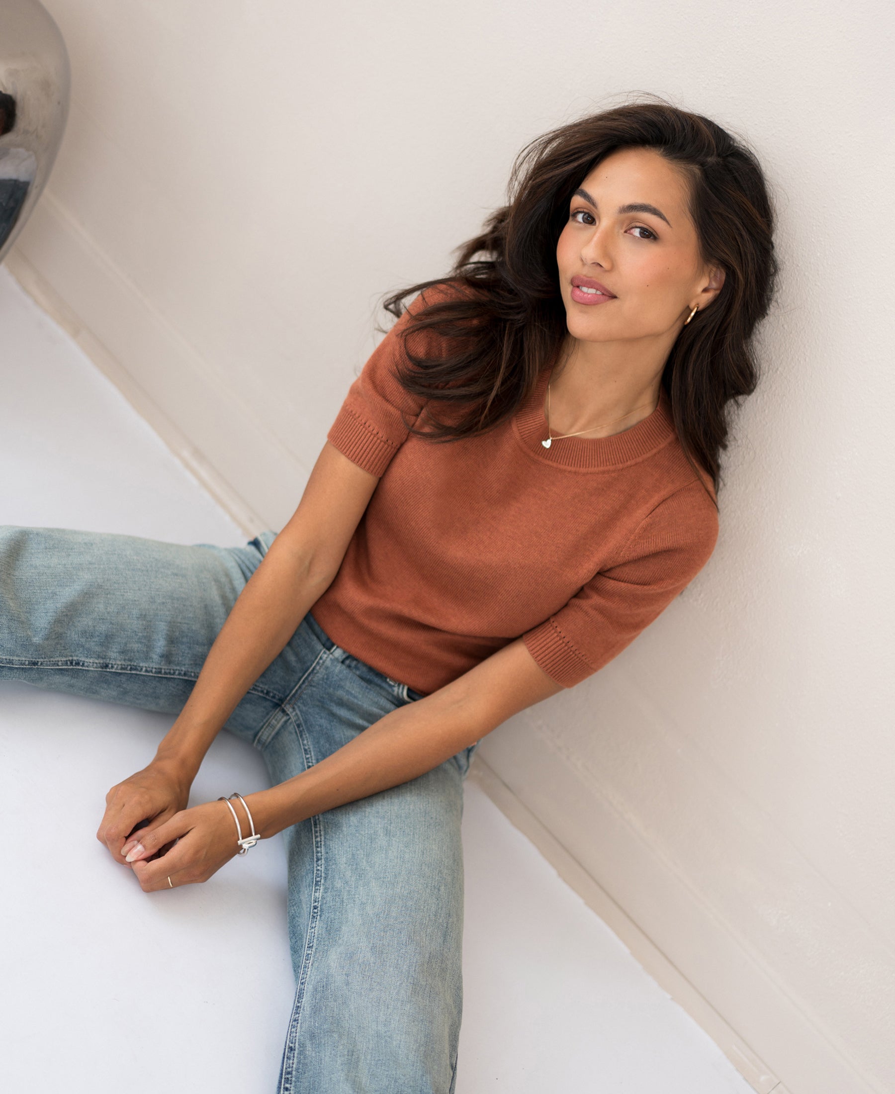 Caramel-colored LA REVE sweater by PLEIN PUBLIQUE shown on a seated woman against a white wall.