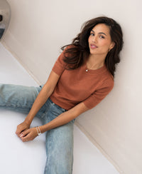 Caramel-colored LA REVE sweater by PLEIN PUBLIQUE shown on a seated woman against a white wall.