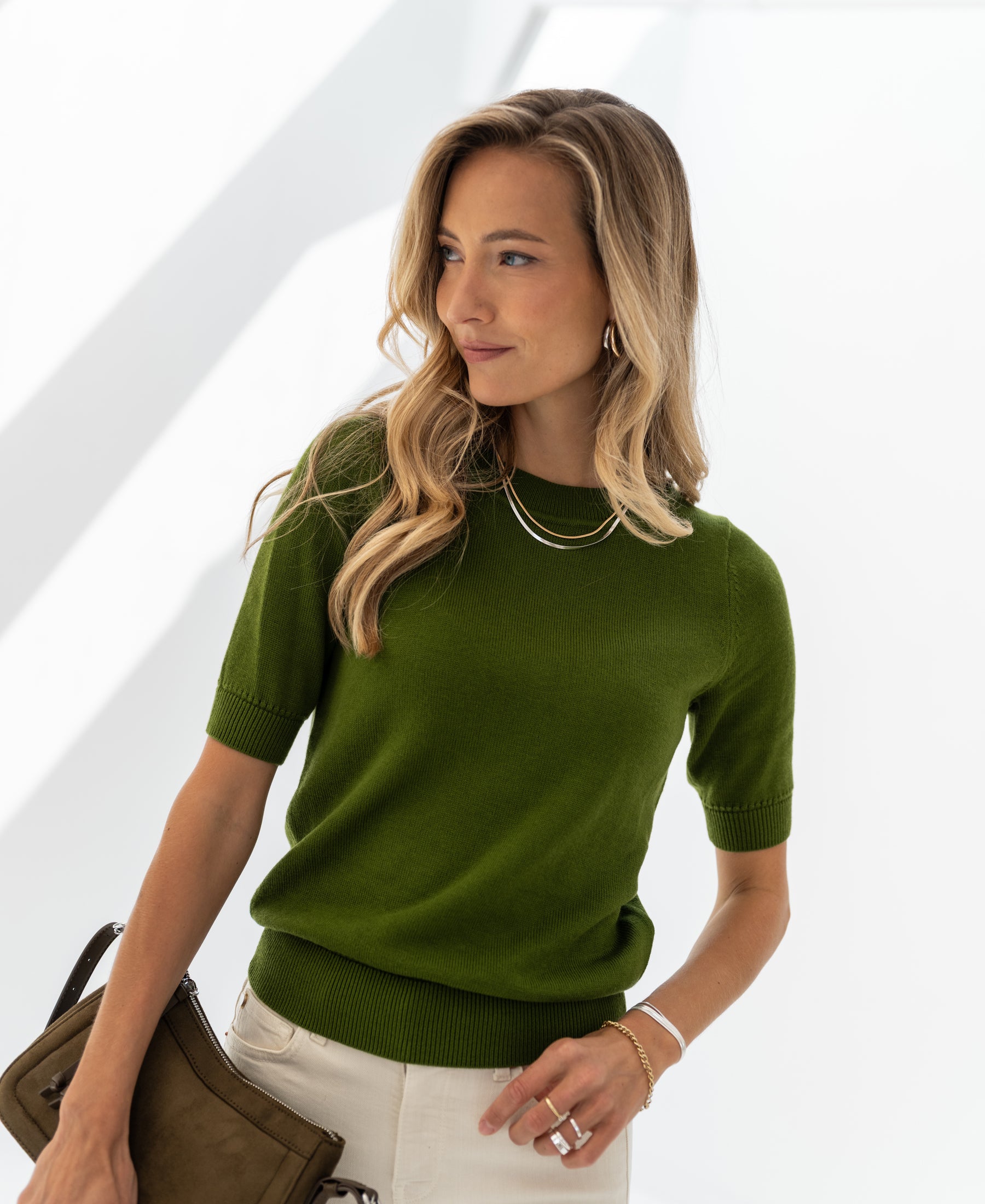 Woman with long blonde hair wearing an olive green PLEIN PUBLIQUE LA REVE sweater.