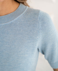 Close-up of a light blue knit sweater with short sleeves and a ribbed crew neck.