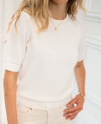 Woman wearing a PLEIN PUBLIQUE LA REVE sweater in off-white, standing indoors.