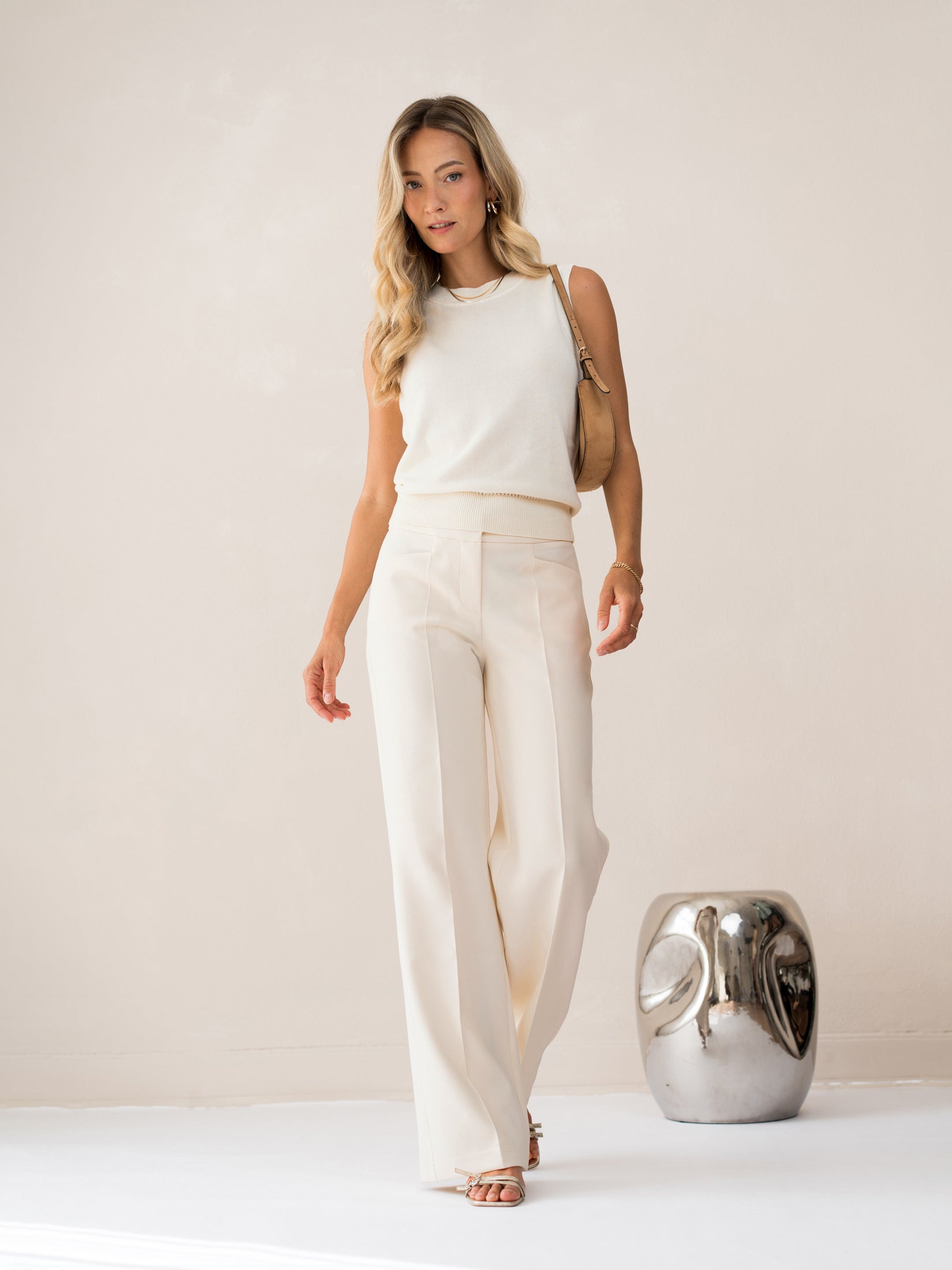 Woman wearing ivory-white LE REVEIL Spencer by PLEIN PUBLIQUE stands indoors near shiny metallic decor.
