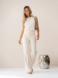 Woman wearing ivory-white LE REVEIL Spencer by PLEIN PUBLIQUE stands indoors near shiny metallic decor.