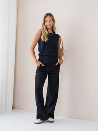 Woman smiles by a light wall wearing a dark blue PLEIN PUBLIQUE LE REVEIL cardigan.
