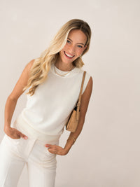 Woman wearing an ivory-white PLEIN PUBLIQUE Spencer LE REVEIL sweater, smiling with hands in pockets.