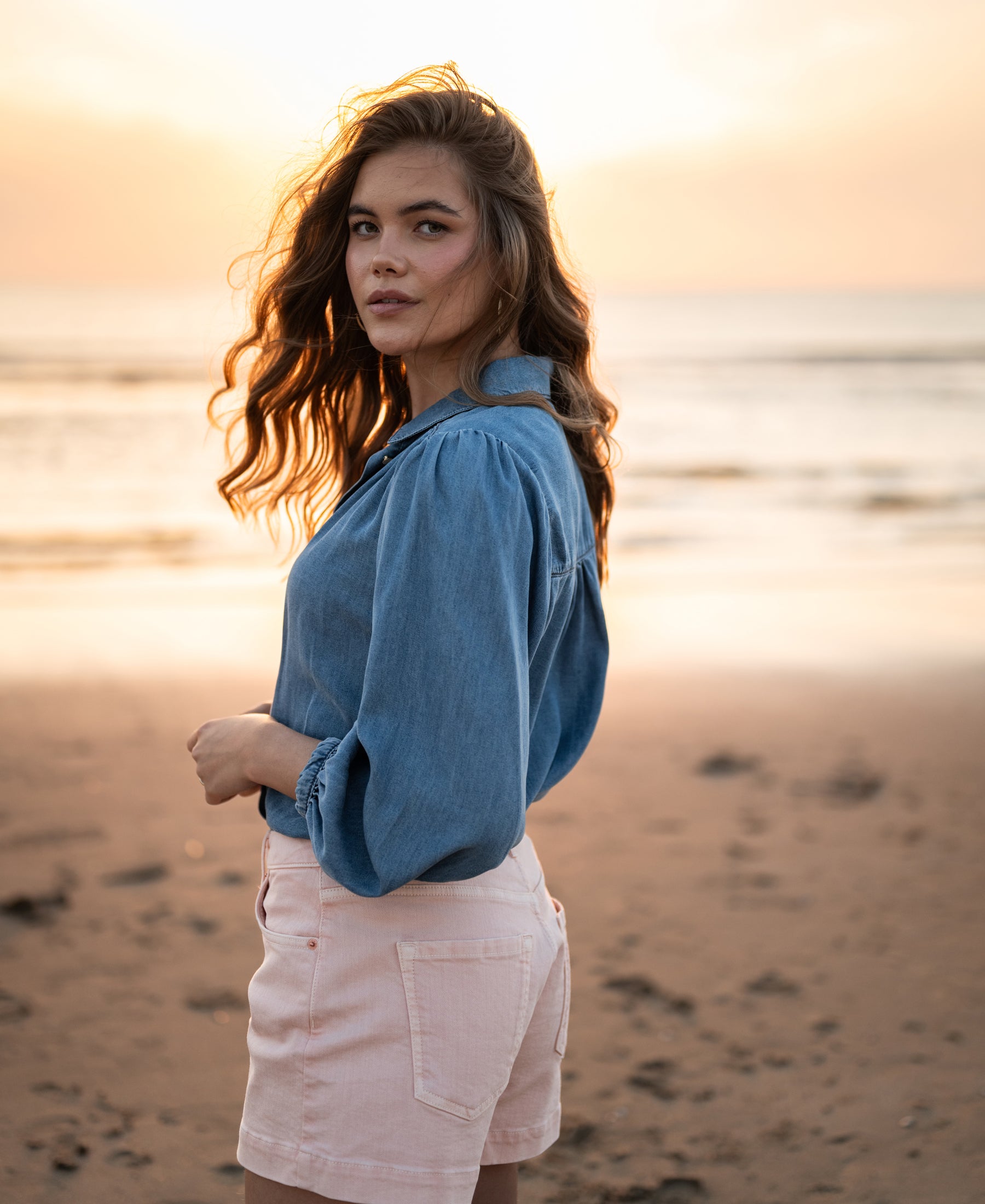 Tencel denim blouse in stonewash, shown on a person at the beach during sunset.