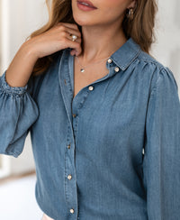 Woman wearing a light blue Tencel denim blouse, stonewashed finish, indoors.