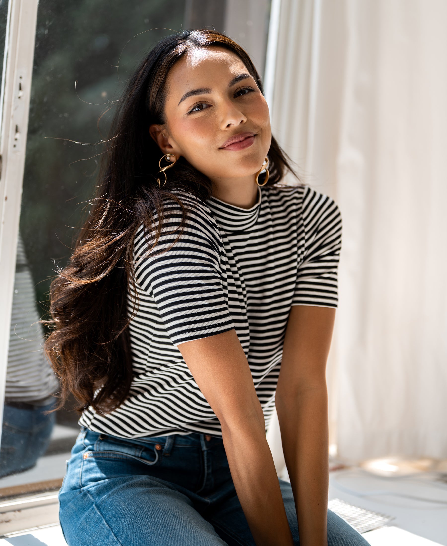 White and black ribbed collared top from PLEIN PUBLIQUE, shown on a woman by a sunlit window.