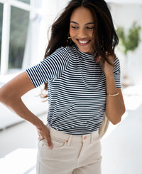 Woman wearing PLEIN PUBLIQUE ribbed collar top, white with dark blue accents, stands indoors with hand on hip.