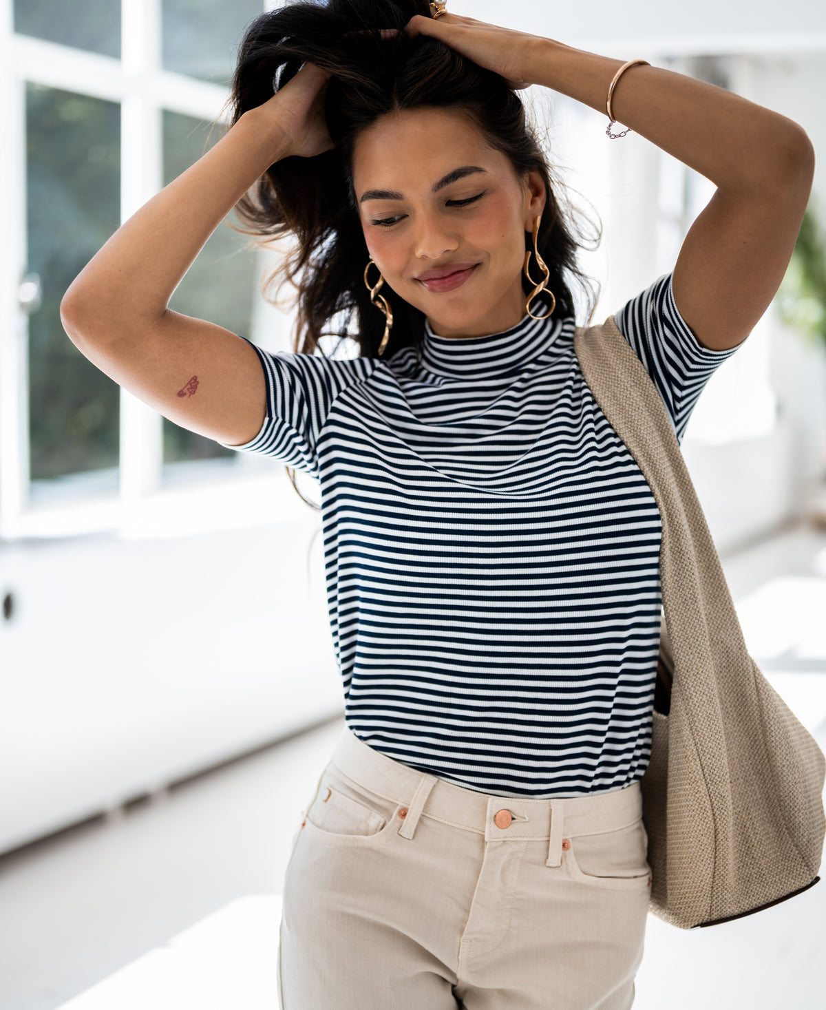 Woman wearing LA RIXY ribbed collared top by PLEIN PUBLIQUE in white and dark blue, hands in hair.