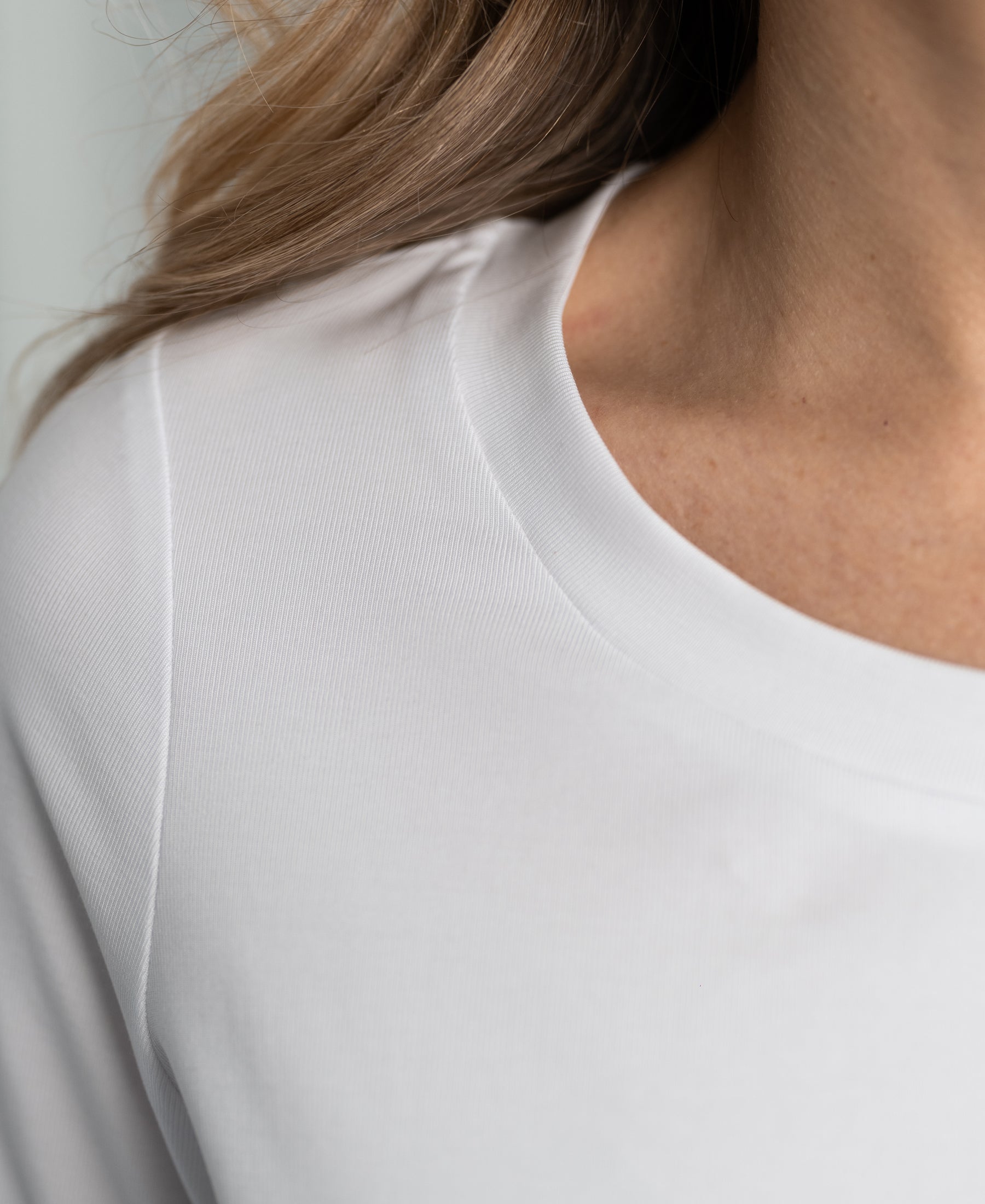 Close-up of a person wearing a white stretch short-sleeve T-shirt, highlighting collar and shoulder.