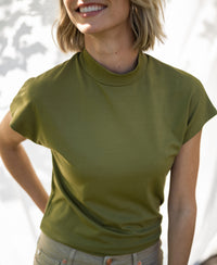Olive green LA ROMY travel blouse by PLEIN PUBLIQUE shown in sunlight, with a softly blurred white background.
