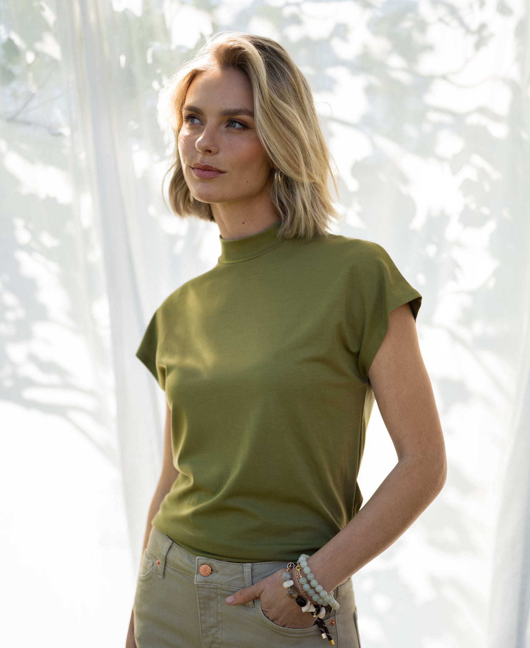 Olive green travel top, viewed outdoors in sunlight and shadows.