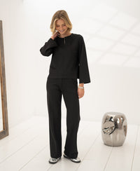 Woman wearing a striped LE SAINT Pure Choco brown top by PLEIN PUBLIQUE, indoors on a white floor.