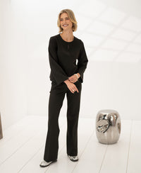 Woman wearing striped top in pure chocolate color, standing in bright white room near metallic stool.