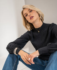 Woman wearing the PLEIN PUBLIQUE LES SALLES anthracite turtleneck sweater, seated and looking at the camera.