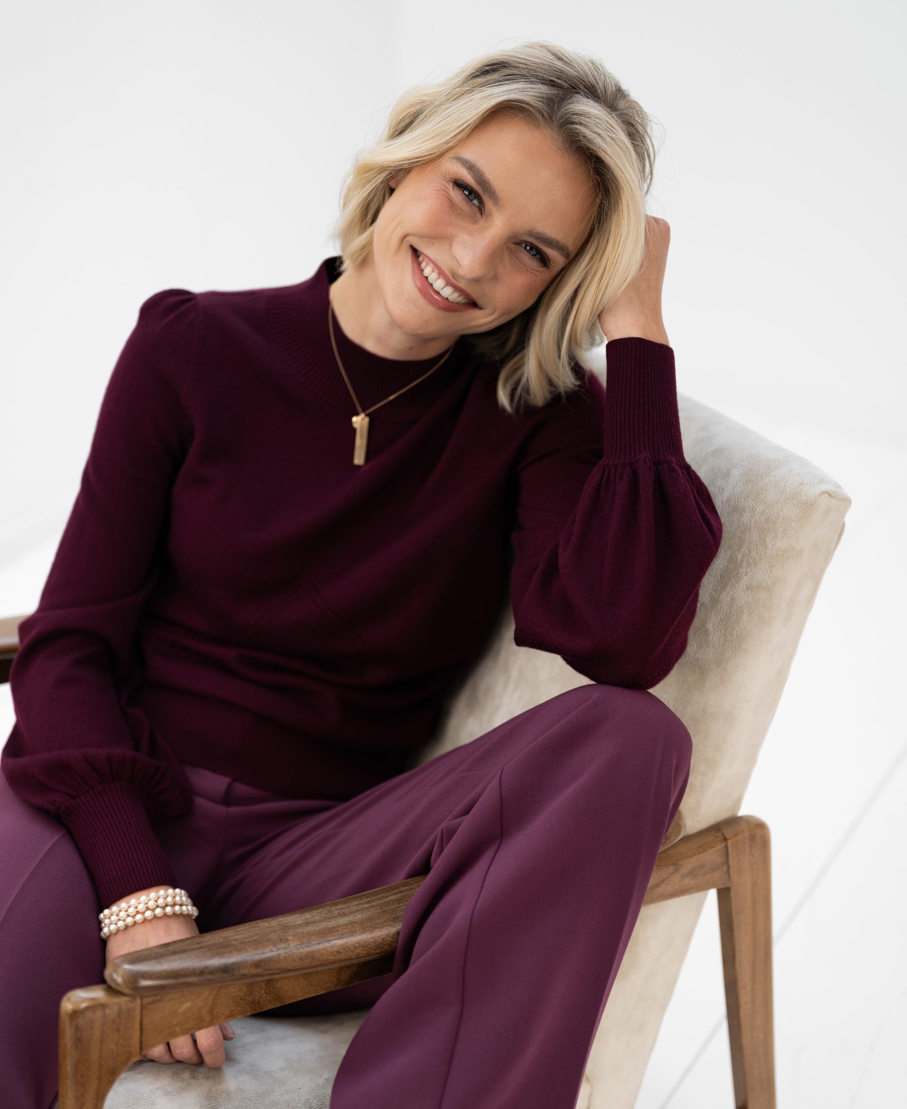 Woman wearing a PLEIN PUBLIQUE turtleneck sweater in Bordeaux red, sitting with head resting on her hand.