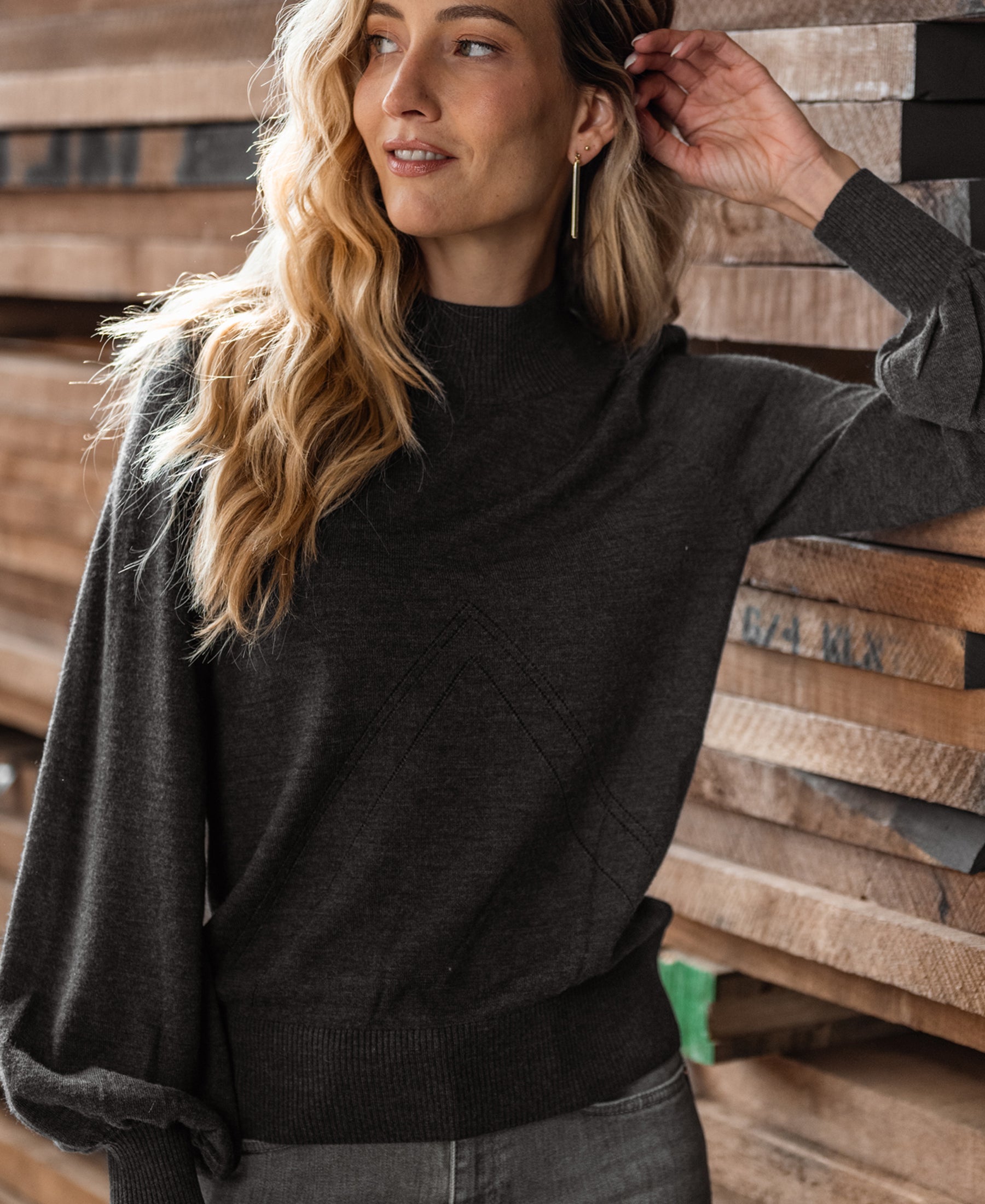 Woman wearing a PLEIN PUBLIQUE anthracite turtleneck sweater, smiling and looking to the side.