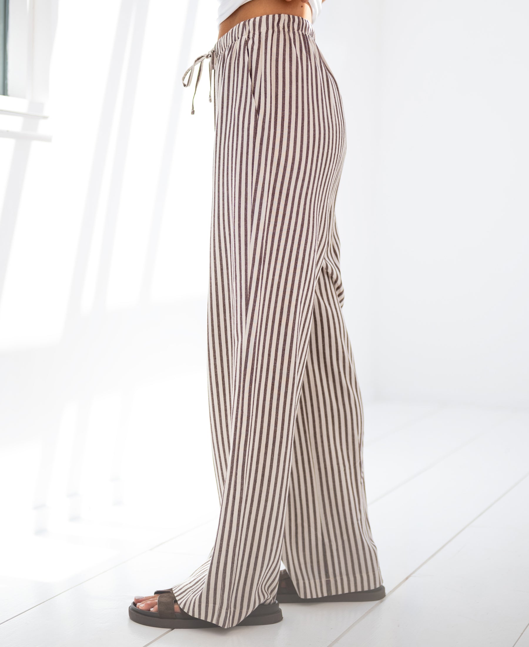Striped brown linen-blend pants by PLEIN PUBLIQUE shown in a bright, sunlit room.