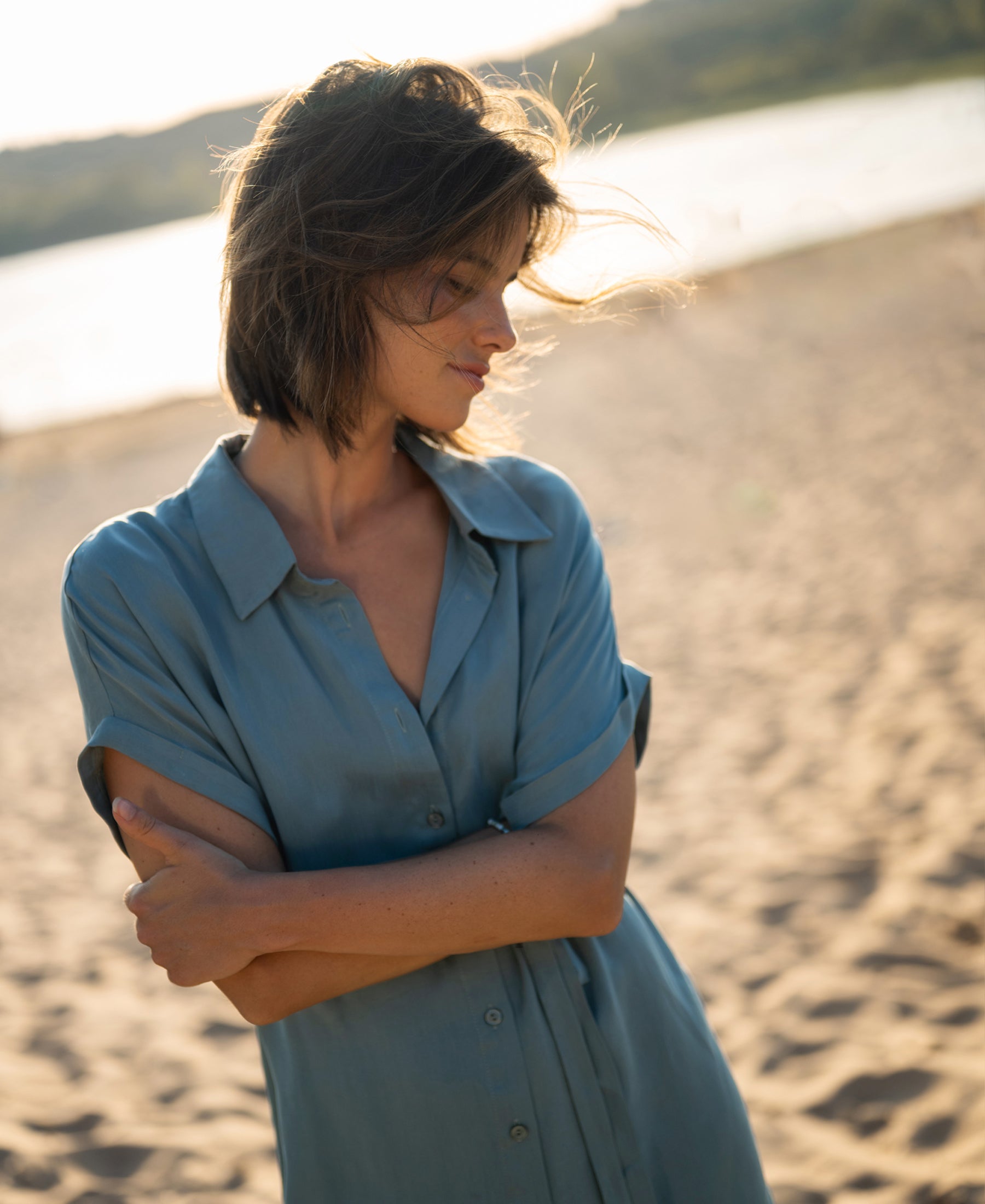 Cupro dress in denim cloud color shown on a model standing on a beach, viewed from the front.