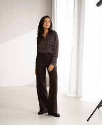 Woman wears a chocolate and ivory polka dot blouse in a bright room with white curtains.