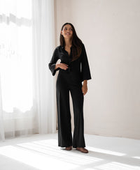 Black PLEIN PUBLIQUE LA JULIA travel pants displayed in a bright, minimalist room.