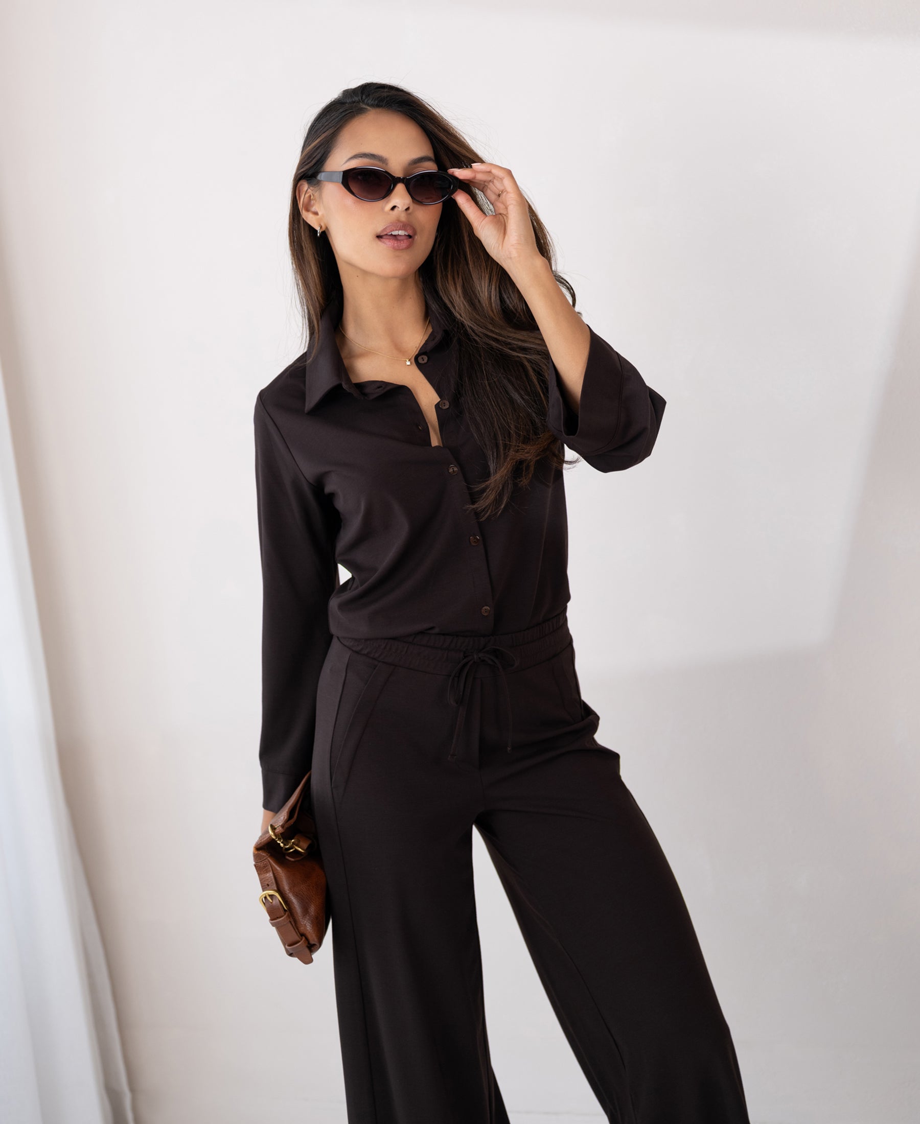Woman poses confidently in a PLEIN PUBLIQUE travel blouse in pure chocolate brown.