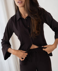 Woman wearing brown travel pants made from pure material stands indoors.