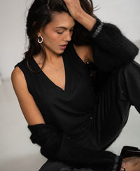 Woman wearing black Lyocell top sits, hand in hair, looking down thoughtfully.