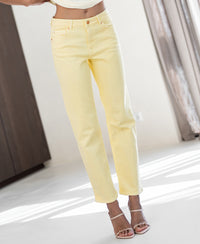 Person wears light yellow cropped jeans, indoors with sheer curtains behind.