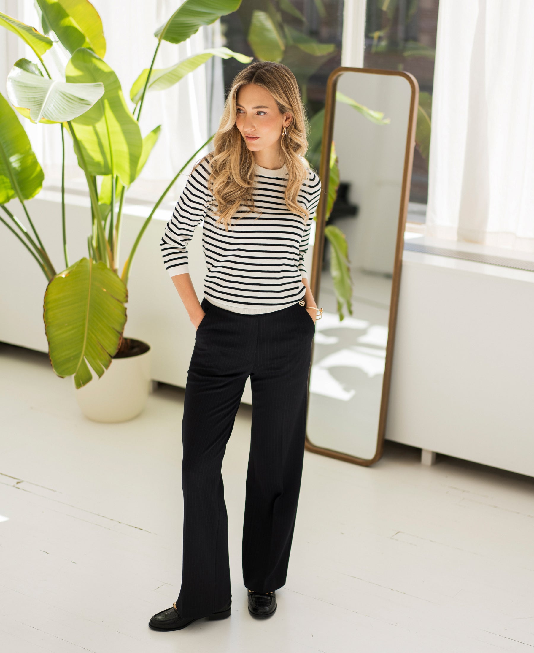 Ivory-black striped LA SITGES sweater by PLEIN PUBLIQUE displayed in a bright room with plants and a floor mirror.