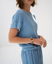 Woman wearing a PLEIN PUBLIQUE summer sweater with linen in light blue, shown in soft light.