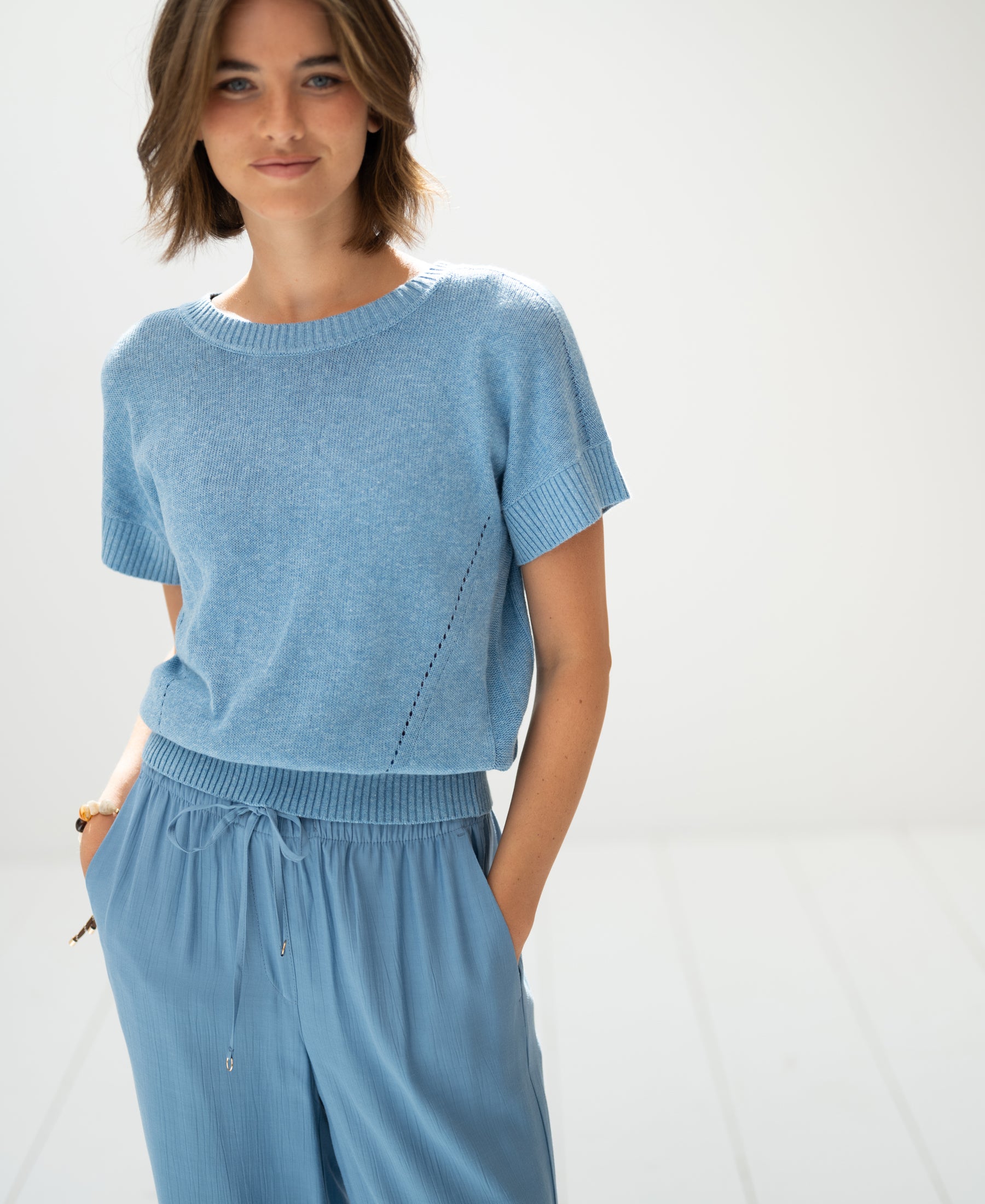 Light blue linen LE SOLEIL summer sweater from PLEIN PUBLIQUE shown in a bright, minimalist room.