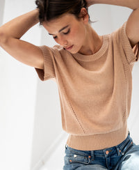 Linen blend summer sweater in soft camel shown with arms raised in soft natural light.
