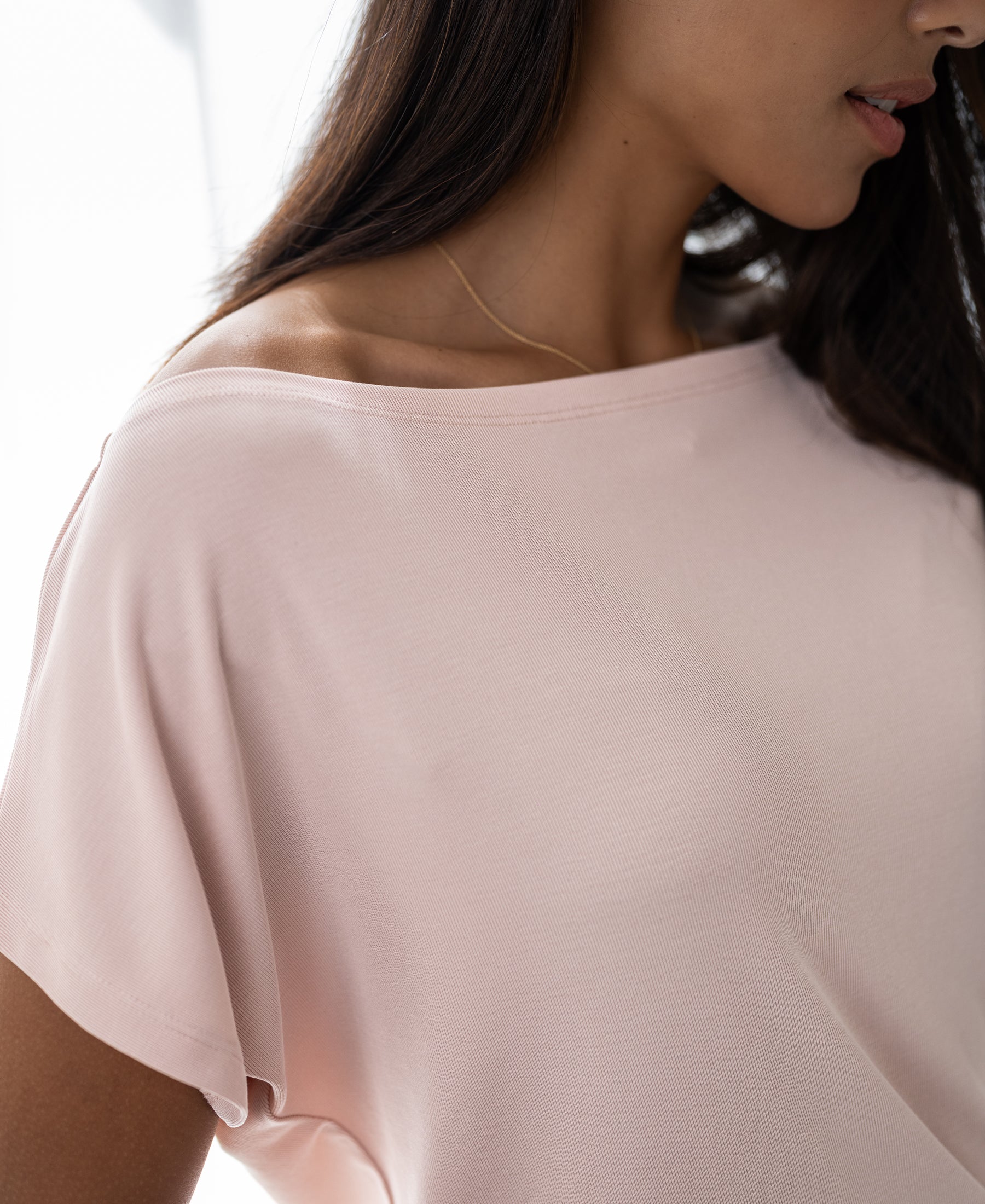 Woman wearing a blush pink ribbed boat neck T-shirt, shown from shoulders down.