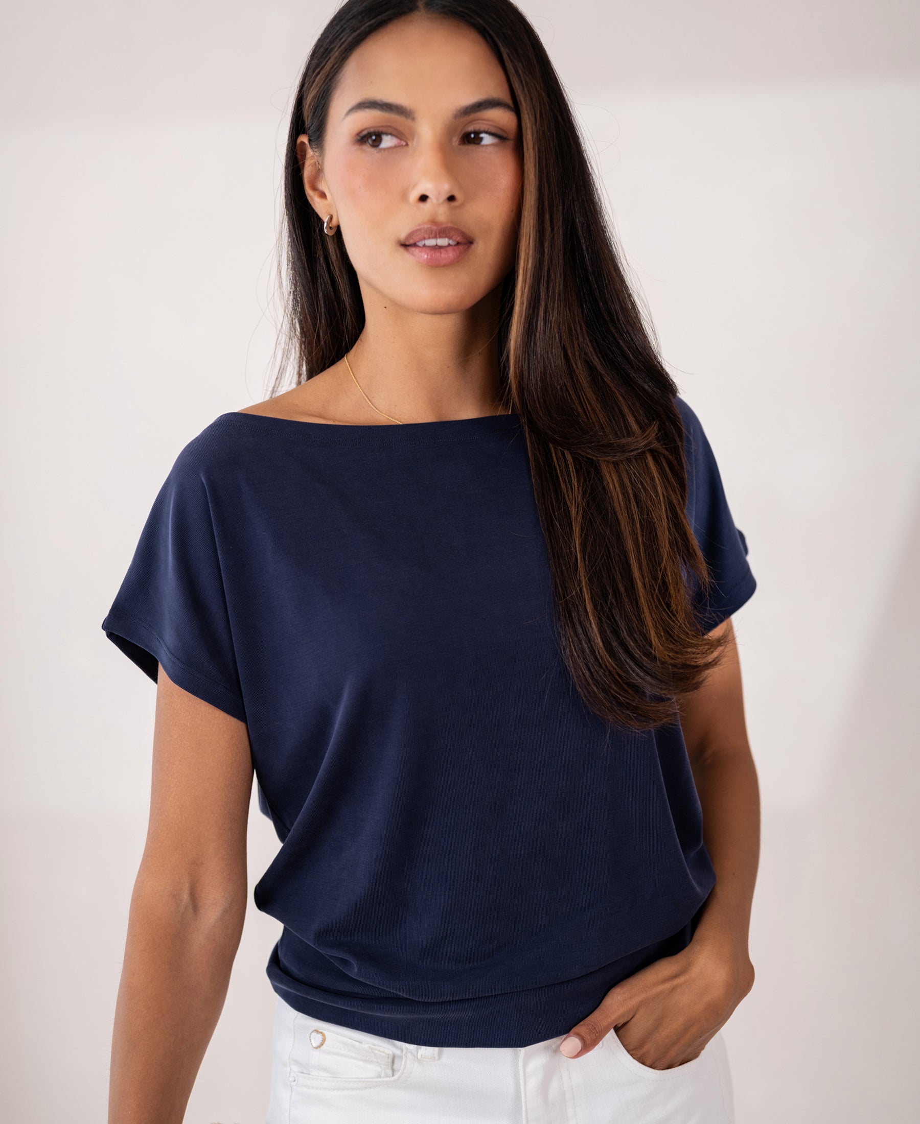 Woman wearing a PLEIN PUBLIQUE rib boatneck T-shirt in dark blue stands against a light background.