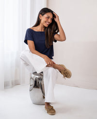 Woman wearing a dark blue ribbed boat neck T-shirt sits on a shiny stool.
