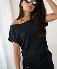 Woman wearing ribbed charcoal boat neck T-shirt stands indoors, looking confidently.
