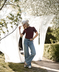 Woman wears a bamboo turtleneck top in red-brown by PLEIN PUBLIQUE, shown outdoors on a sunny day.