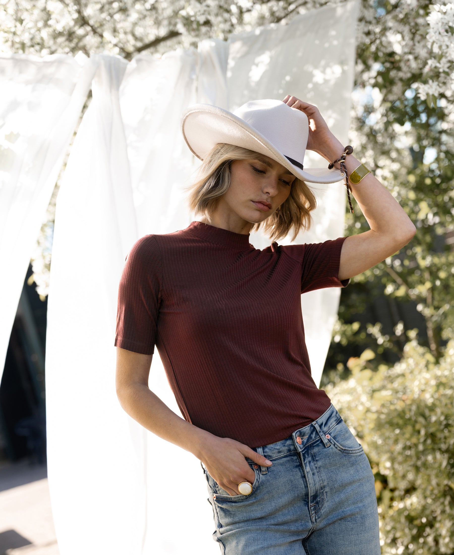 Woman wearing a bamboo turtleneck top in red-brown outdoors by blooming trees.