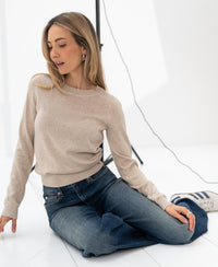 Woman wearing the Merino sweater LE SONGE Sand from PLEIN PUBLIQUE, seated on the floor in a bright studio.
