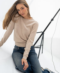 PLEIN PUBLIQUE LE SONGE sand-colored merino wool sweater shown on a woman, seated on white floor with studio lighting.