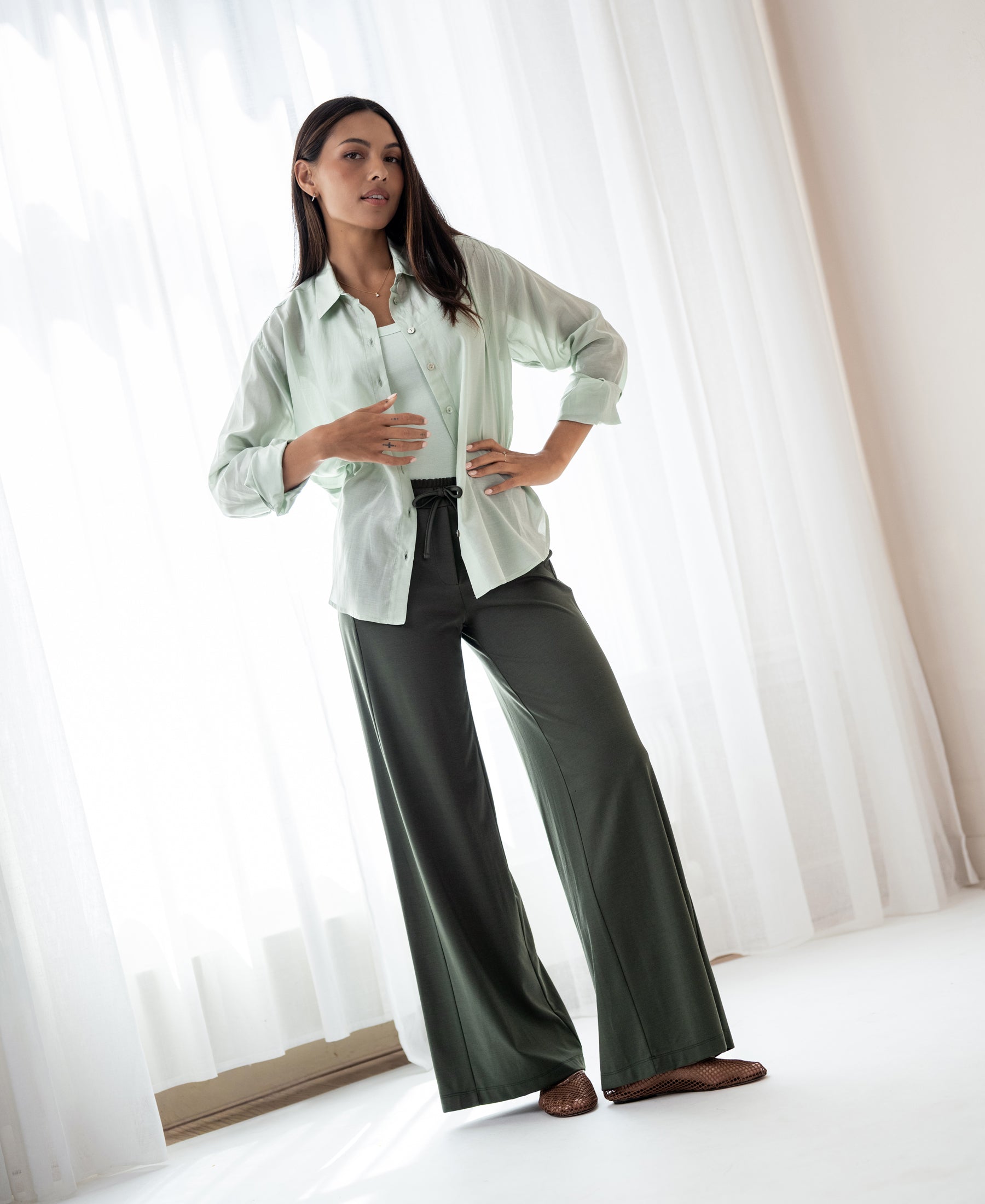 Oversized light green blouse in silky fabric from PLEIN PUBLIQUE, shown indoors near white curtains.