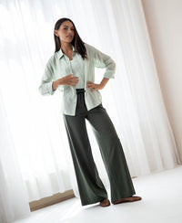 Oversized light green blouse in silky fabric from PLEIN PUBLIQUE, shown indoors near white curtains.