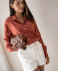 Woman wearing oversized Terra-colored LA SOYEUSE blouse by PLEIN PUBLIQUE, standing against a light wall.