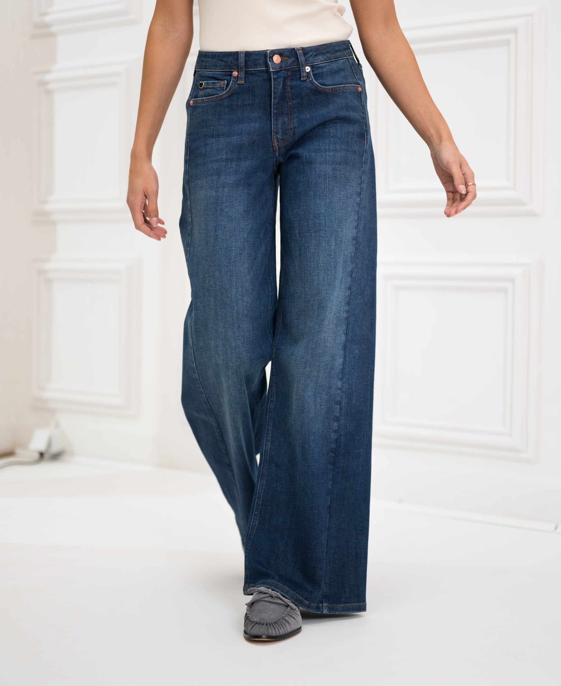 Wide leg blue heritage jeans in a classic style, shown standing by a white paneled wall.