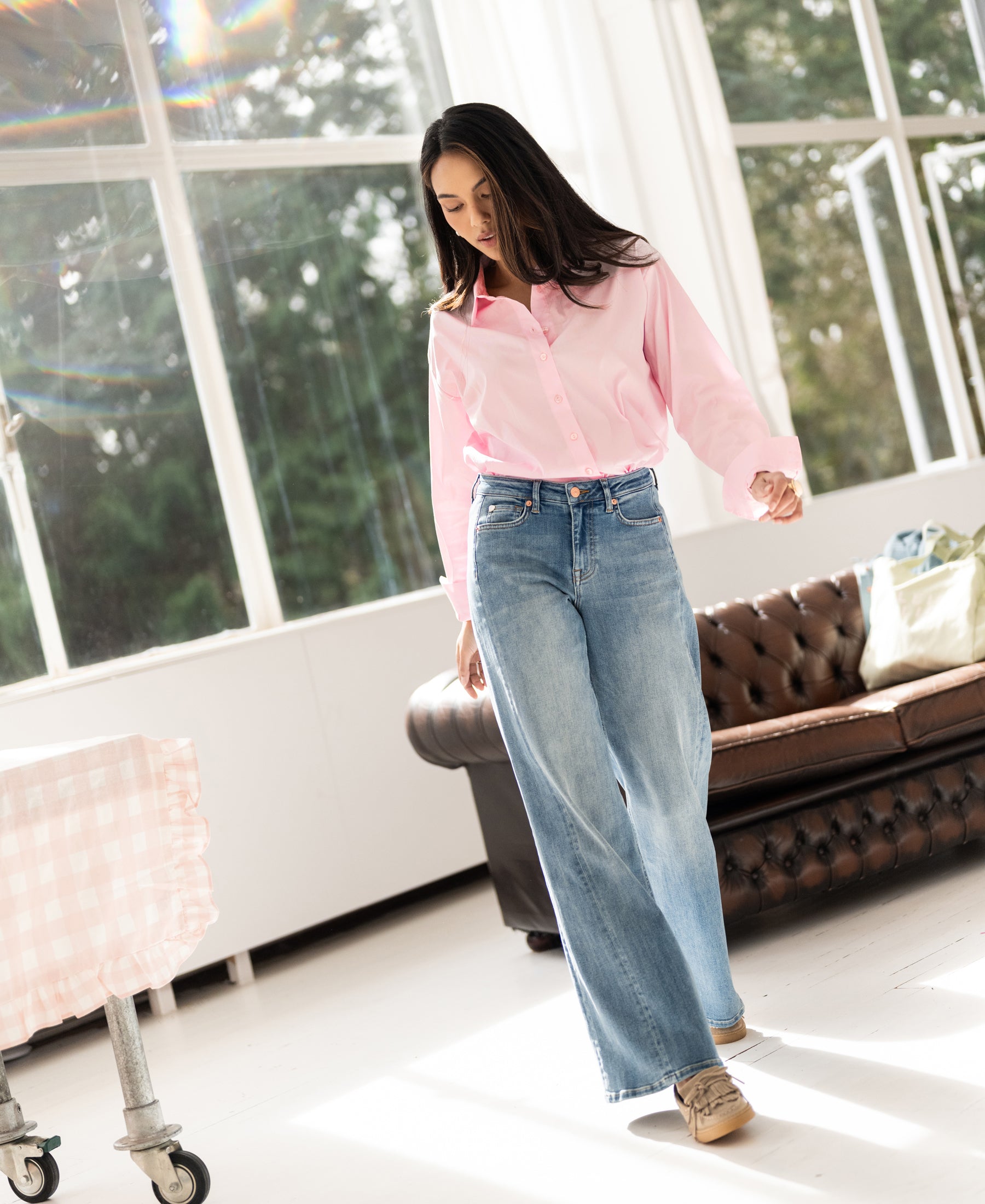 Wide leg light stone wash jeans displayed indoors by a brown sofa and sunlit windows.