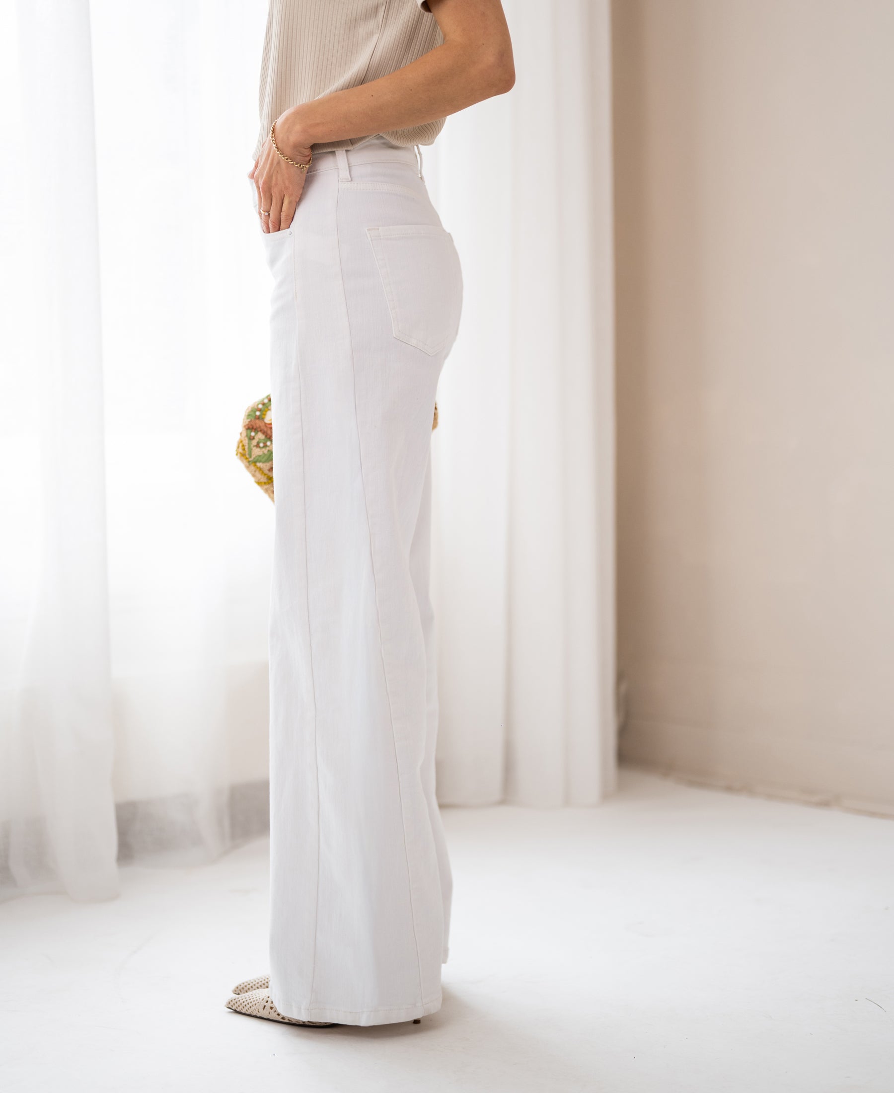 Wide leg white jeans shown from the side in a bright, minimalist room.