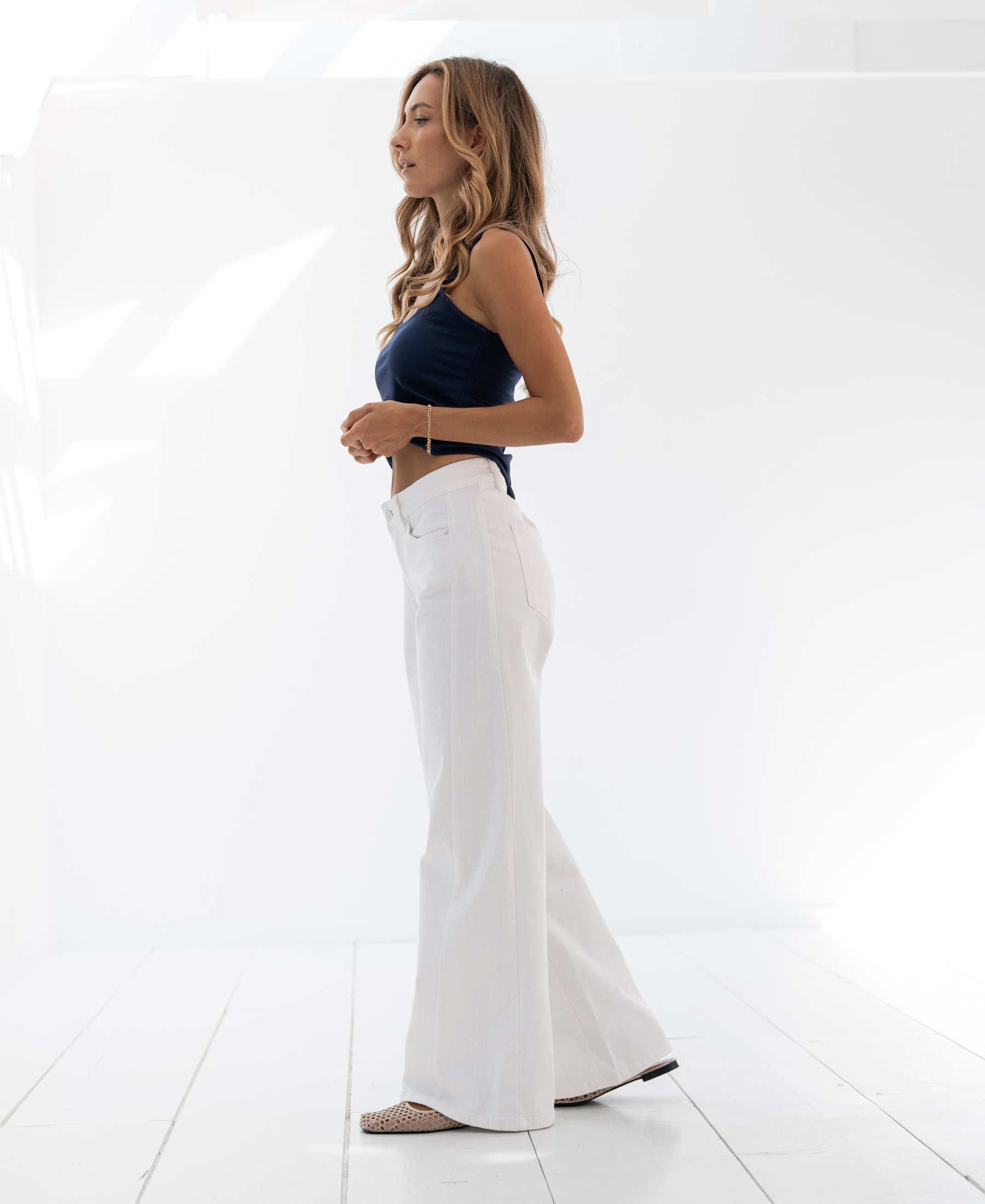 Wide leg white jeans shown in profile in a bright white room.